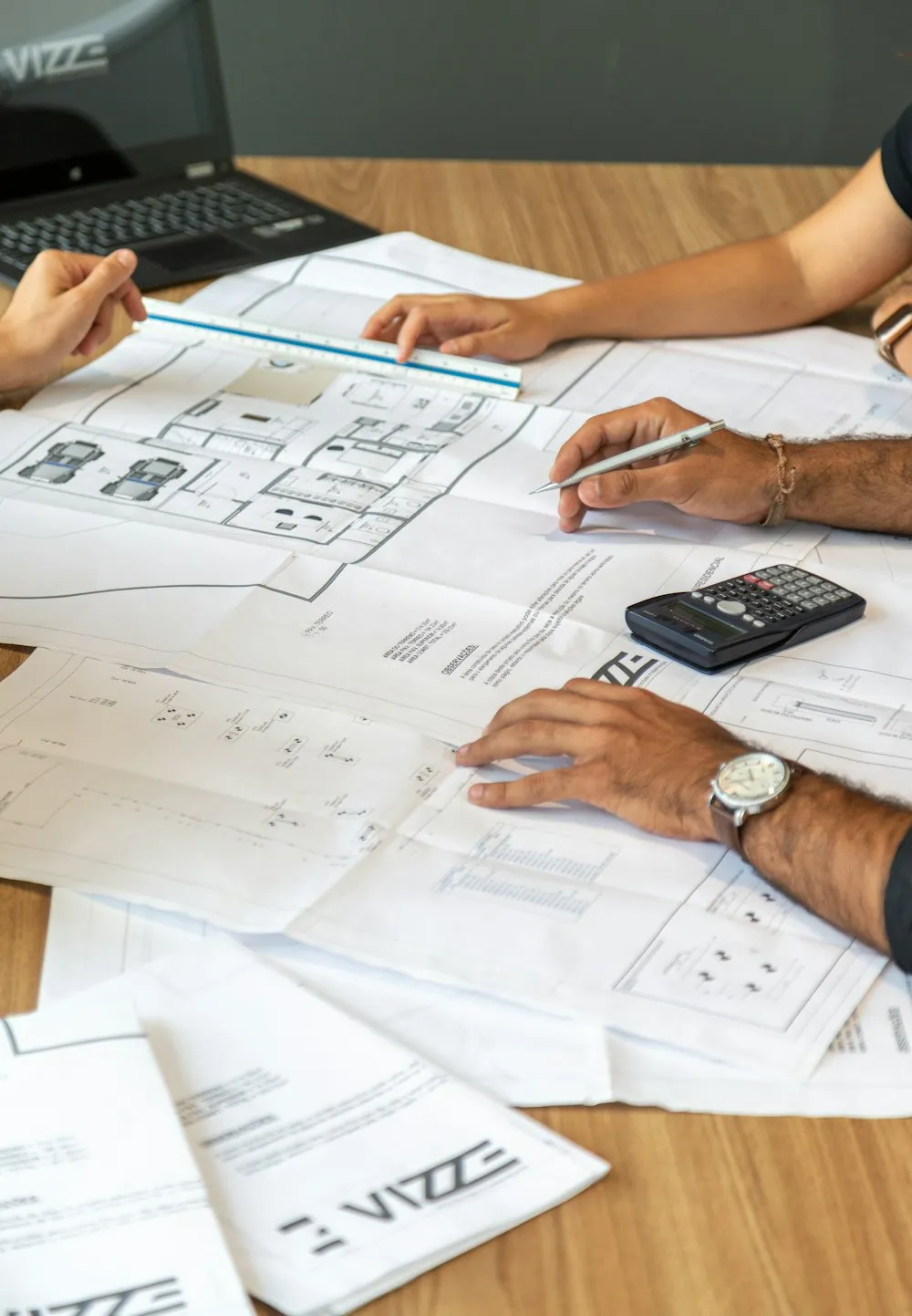 Dos personas revisando planos de obra sobre una mesa, con calculadora y escalímetro
